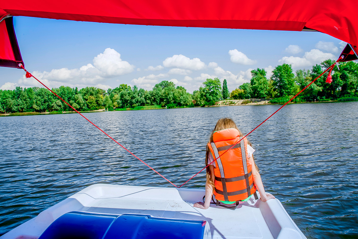 Young girl wearing life vest sitting at the back of a boat on the lake
